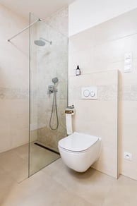Moderní koupelna se sprchovým koutem a závěsným WC v béžových tónech.
